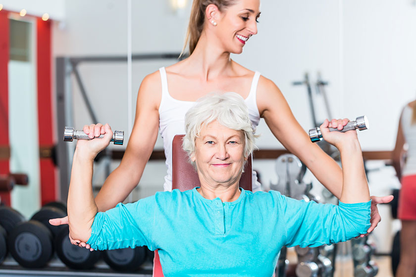 Senior woman with trainer in gym lifting dumbbell