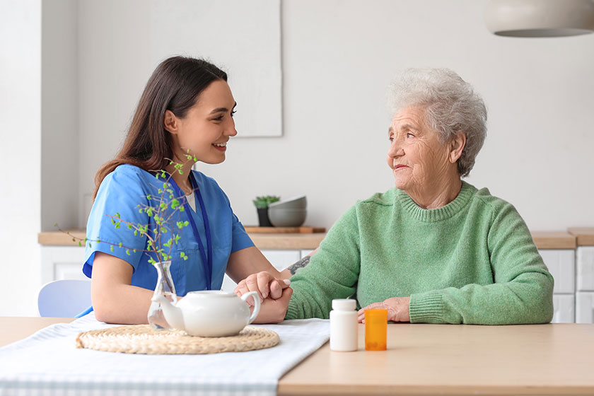 Young caregiver with senior woman holding hands in kitchen